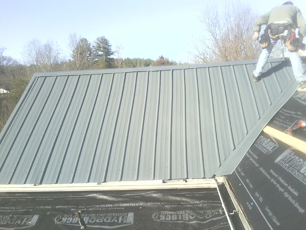 Crew installing dark green standing seam panels over synthetic underlayment in Hahira