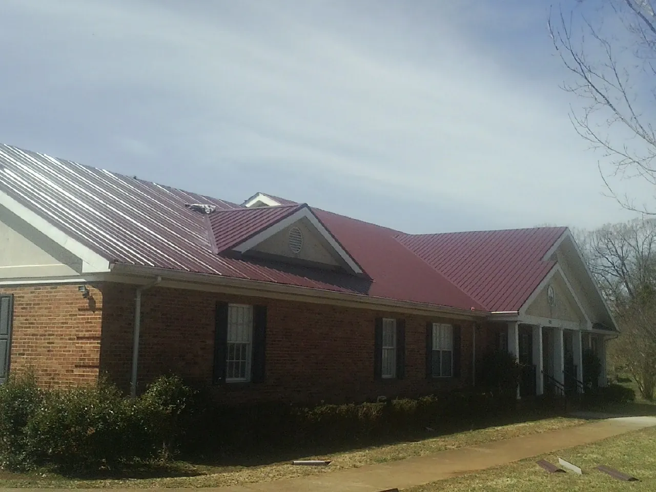 Red metal roof with gabled entries on a long brick building, from a Hail Damage Roof Repair job in Hahira