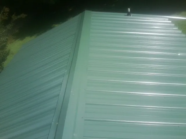 New green metal panels meeting at the ridge of a roof — Flat Roof Repair work by our crew in Hahira