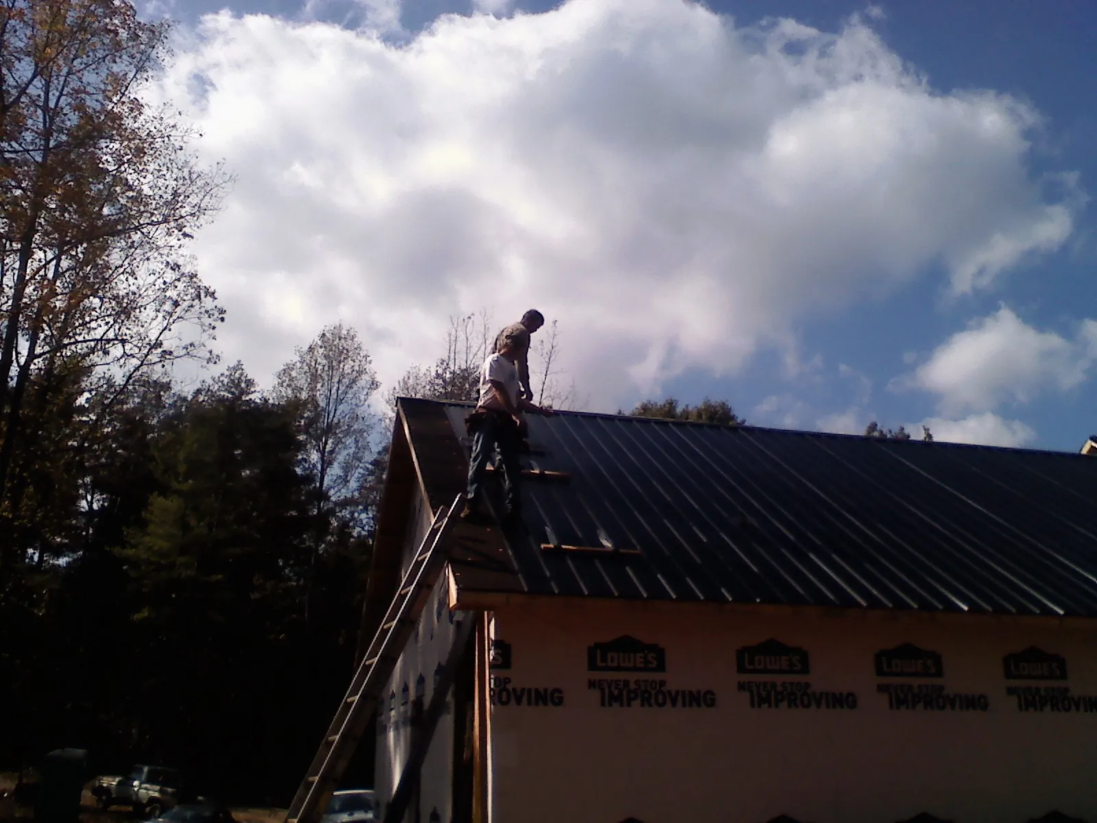Roofer fastening dark metal panels high against a cloudy sky, from a Roof Inspection job in Hahira