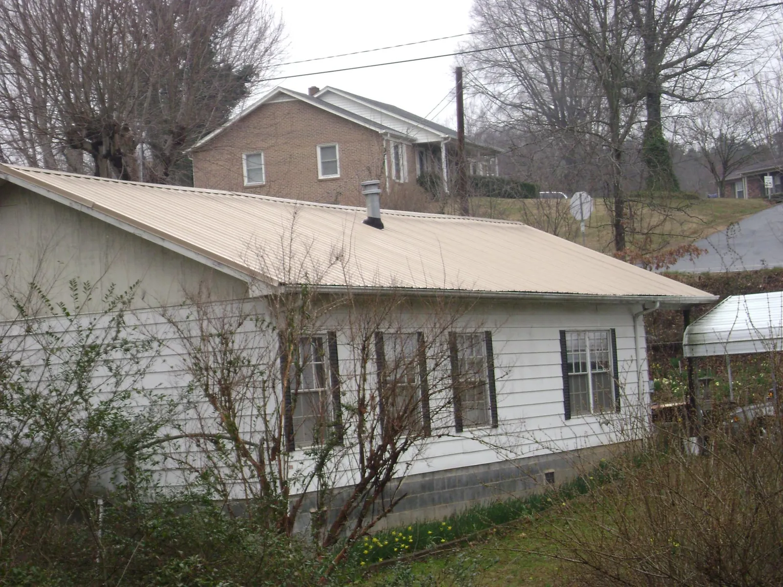 Tan metal roof on a white sided house set into a hillside — Commercial Roofing by Roofing Brothers in Hahira