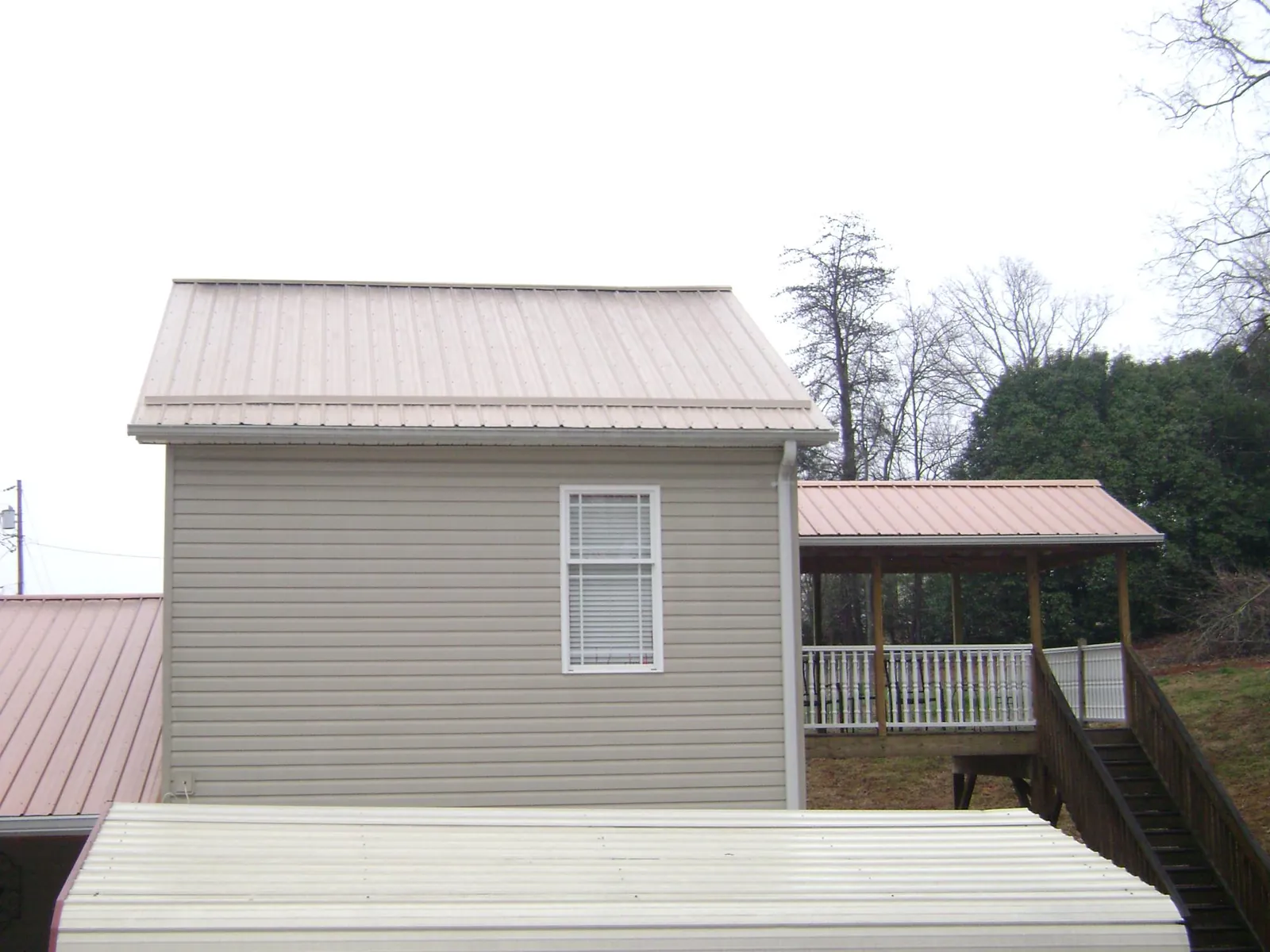 Tan metal roofs on a two story addition and attached porch, from a Roof Replacement job in Hahira